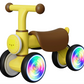 The Freddo Nature Navigator Balance Bike for toddlers features a yellow and brown design, a playful lion face on the front, and illuminated multicolored LED lights in the wheels for enhanced sensory discovery, shown on a white background.