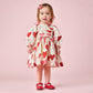 A toddler girl poses against a pink background in the Pink Chicken Baby Girls' Renee Dress Set with gradient hearts, paired with red shoes and a matching bow—an adorable choice for Valentine’s Day.