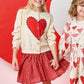 Two young girls wearing Pink Chicken Girls' Gianna Skirts and heart print Valentine’s Day outfits smile in front of a pink and red heart backdrop.