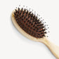 A close-up of the Machete Petite Travel Hair Brush, featuring dark detangling bristles and a light-colored bio-acetate handle, set against a plain white background.