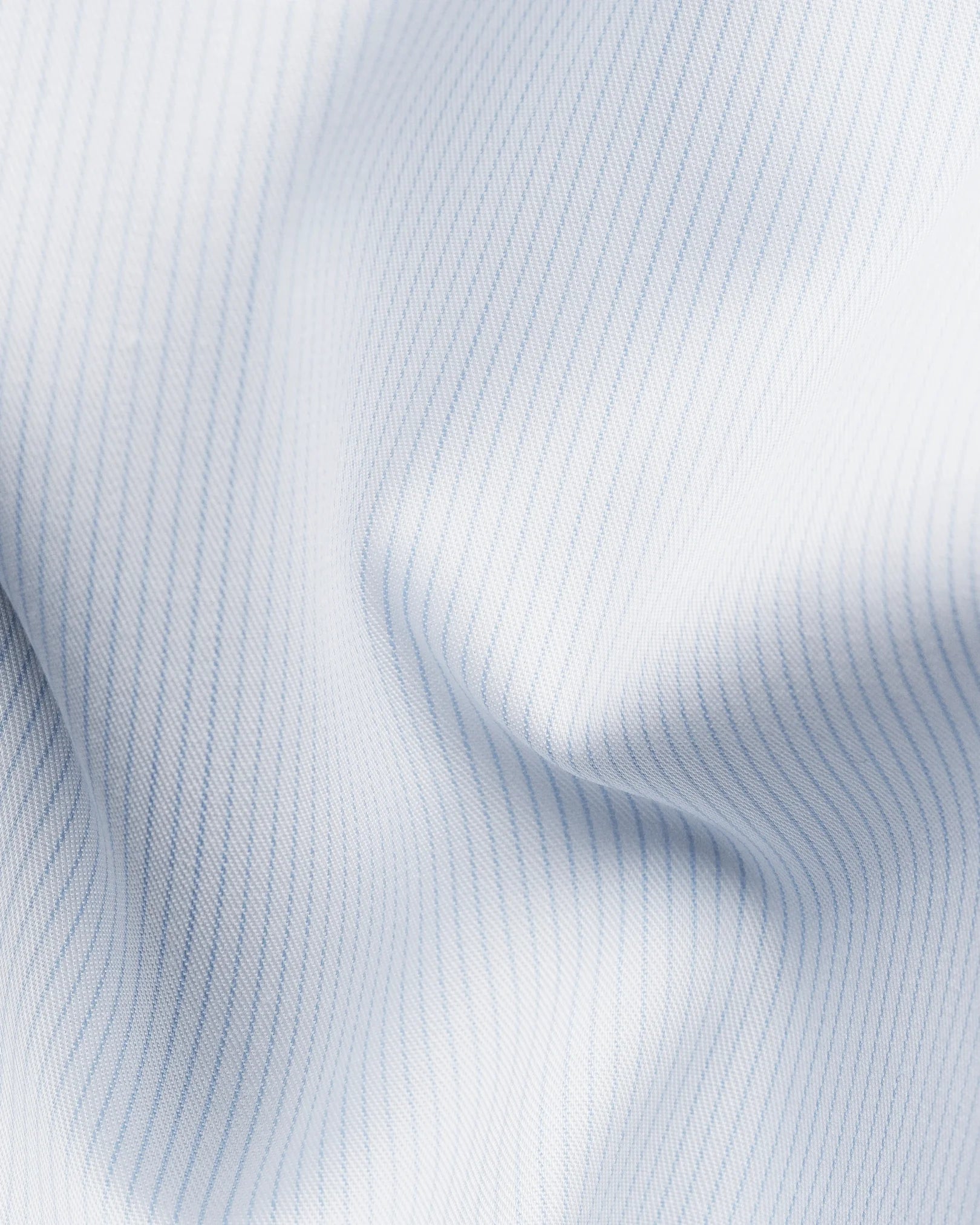 Close-up of the Contemporary Striped Twill Shirt by Eton, featuring light blue and white pinstripe 100% cotton fabric with gentle folds, soft texture, diagonal twill lines, and subtle shadows—a wrinkle-resistant choice ideal for dress shirts.