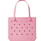 A pink, rectangular Baby Bogg® Bag tote from Bogg Bags features round holes on all sides and two handles. The word “bogg” is embossed on the lower right corner. This washable bag is ideal for everyday adventures and can be easily customized to reflect your unique style.