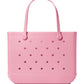 The Original Bogg® Bag by Bogg Bags is a large pink beach tote, featuring two sturdy handles and signature circular holes on both sides. It stands upright on a white background, with the embossed “bogg” logo near the bottom right corner, showcasing this stylish and washable bag’s distinctive design.