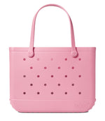 The Original Bogg® Bag by Bogg Bags is a large pink beach tote, featuring two sturdy handles and signature circular holes on both sides. It stands upright on a white background, with the embossed “bogg” logo near the bottom right corner, showcasing this stylish and washable bag’s distinctive design.