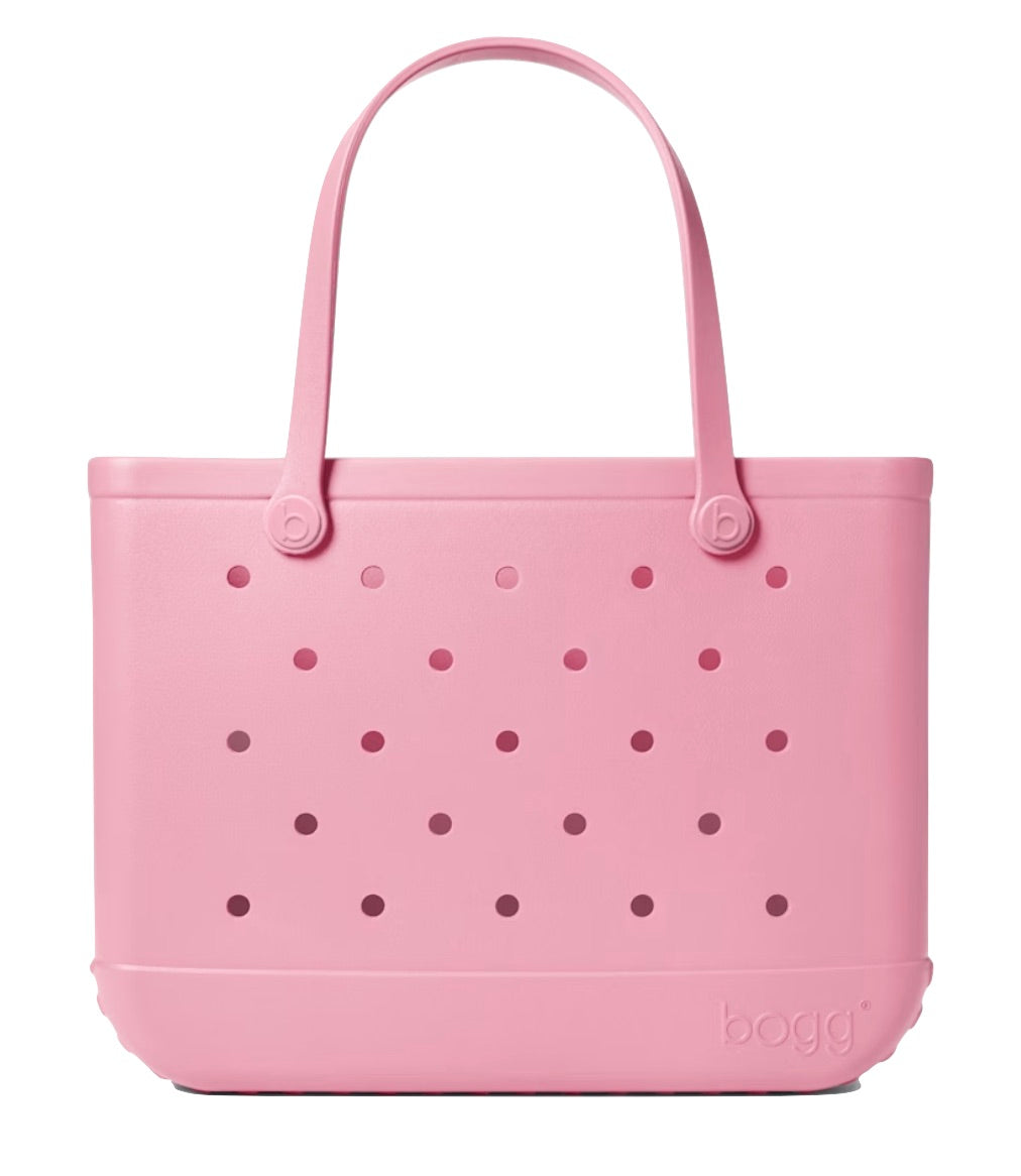 The Original Bogg® Bag by Bogg Bags is a large pink beach tote, featuring two sturdy handles and signature circular holes on both sides. It stands upright on a white background, with the embossed “bogg” logo near the bottom right corner, showcasing this stylish and washable bag’s distinctive design.