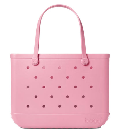The Original Bogg® Bag by Bogg Bags is a large pink beach tote, featuring two sturdy handles and signature circular holes on both sides. It stands upright on a white background, with the embossed “bogg” logo near the bottom right corner, showcasing this stylish and washable bag’s distinctive design.