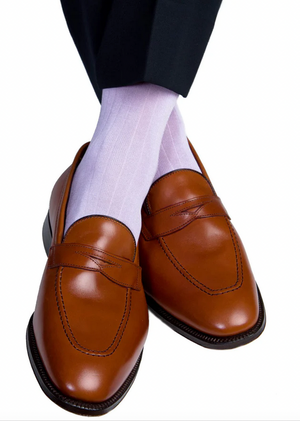 A person wearing Dapper Classics Lavender Solid Ribbed Cotton Sock Linked Toe Mid-Calf and brown leather loafers with black trousers, ankles crossed on a white background.