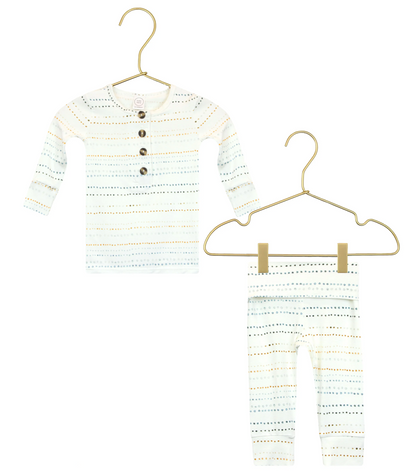 The Lou Lou & Company Baby Conrad Top & Bottoms set features a long-sleeve shirt with buttons and matching pants, both in white with small colored dotted stripes. Crafted from silky-soft fabric, the pants have a fold-over waistband and built-in footies for extra comfort. The set is displayed on gold hangers against a white background.