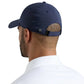 A man shown from behind wears a navy blue Peter Millar Pursuit Performance Hat with an adjustable elastic loop closure and a white collared shirt.
