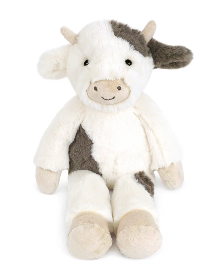 Ida Cow by Mon Ami is a cuddly cow plush with white and brown patches, a beige snout, and a small smile, sitting upright against a plain white background.