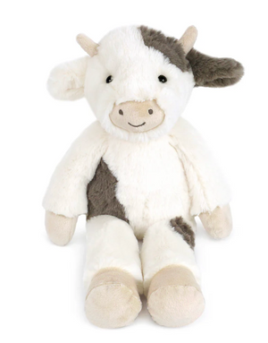 Ida Cow by Mon Ami is a cuddly cow plush with white and brown patches, a beige snout, and a small smile, sitting upright against a plain white background.