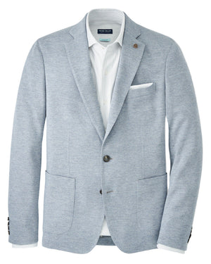 The Peter Millar Barclay Knit Soft Jacket in light gray-blue features a relaxed fit, two front pockets, a chest pocket with white pocket square, dark buttons, and is styled over a white collared shirt.
