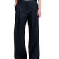 Someone wearing the Proenza Schouler White Label Coralie Pant—loose-fitting, high-waisted, wide-leg with front pleats and pockets—paired with a black top and open-toe black sandals.