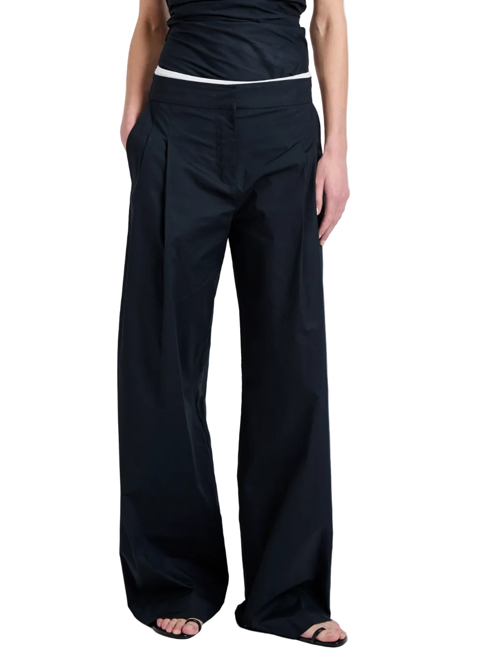 Someone wearing the Proenza Schouler White Label Coralie Pant—loose-fitting, high-waisted, wide-leg with front pleats and pockets—paired with a black top and open-toe black sandals.