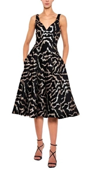 A woman is wearing a Prabal Gurung V Neck Fit & Flare Dress in black, showcasing a breathtaking silver abstract pattern with metallic gold accents, paired flawlessly with black high-heeled sandals.