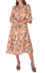 A person showcases the Prabal Gurung Button Sleeve Shirtdress featuring a vibrant floral print in orange, green, and pink hues, paired elegantly with beige sandals.