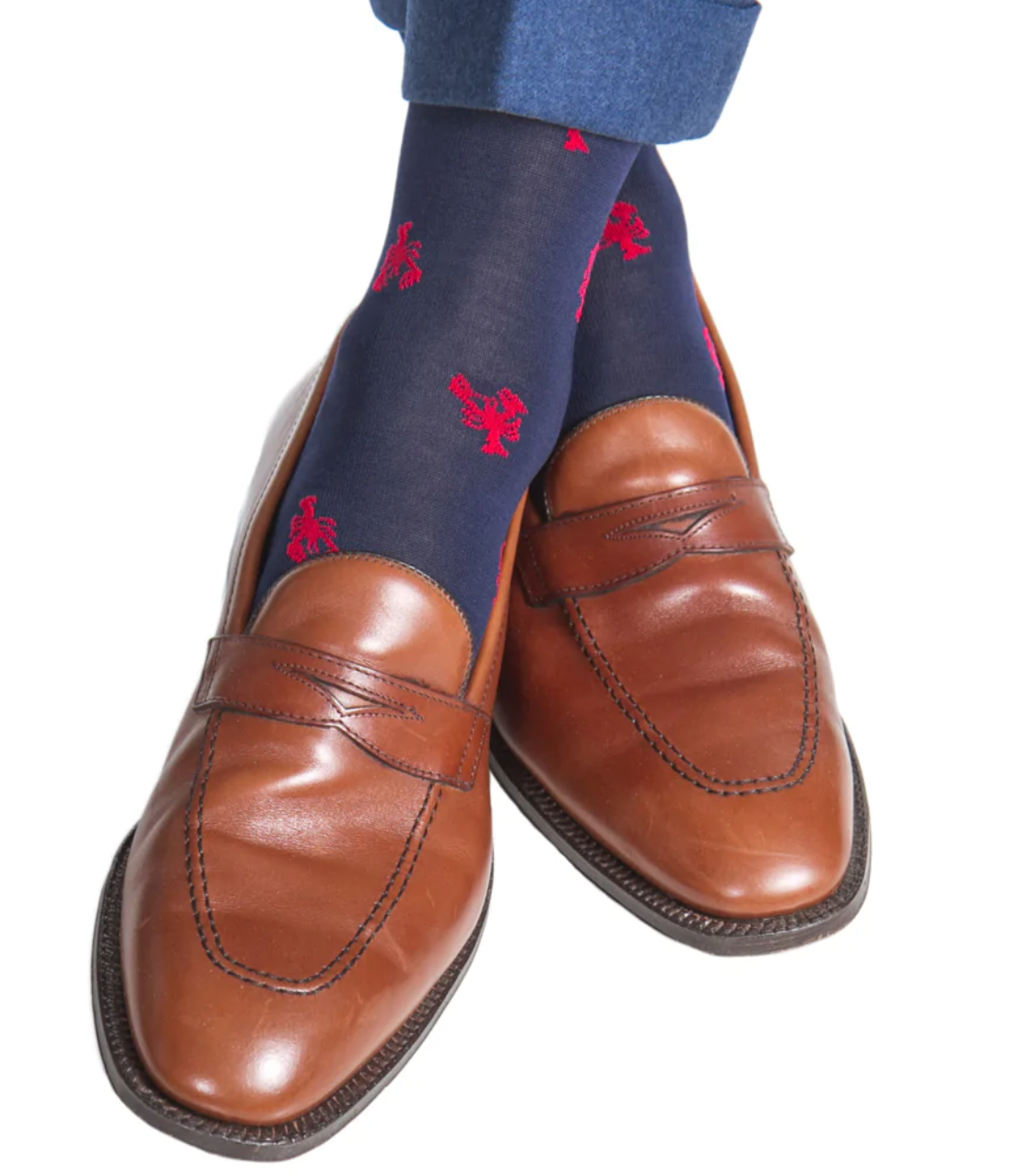 The individual exudes charm, donning brown leather loafers crafted with breathable material. Paired with navy mid-calf socks featuring a whimsical red lobster pattern from Dapper Classics, these linked-toe accessories add a touch of playful sophistication.