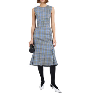 A woman wears the Proenza Schouler Bruna Plaid Wool Nylon Dress—sleeveless and blue-and-white, styled with black tights, white heels, and a black cylindrical clutch against a white background.