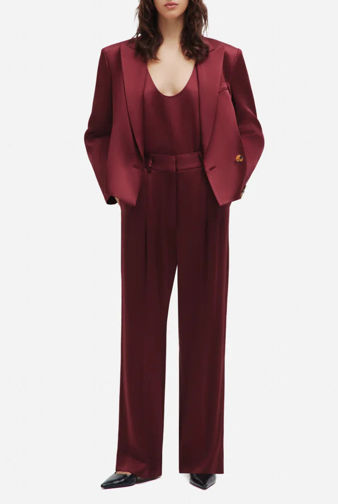 A person wears Blaze Milano’s Novalis Fox Pants in burgundy satin with a matching blazer and top, styled with black pointed shoes.