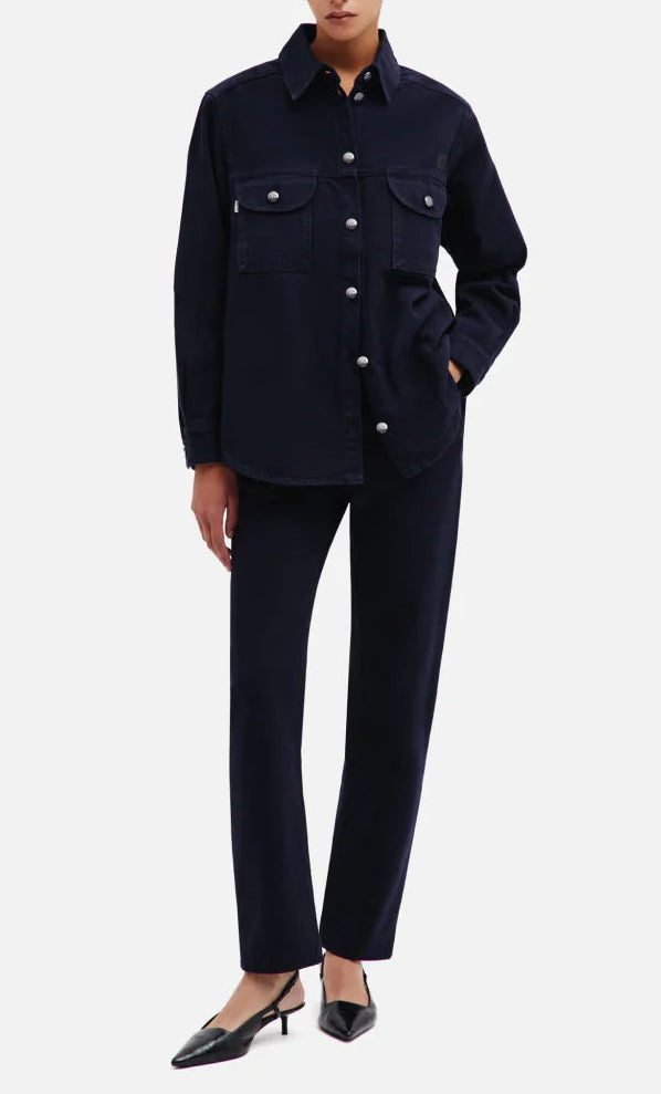 A person wearing a dark button-up jacket with front pockets, paired with the Blaze Milano Clapotis Paso Jeans in a matching dark blue straight-leg style and black pointed-toe heels, stands with one hand in their pocket.