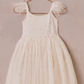 The Noralee Girls' Poppy Dress—a white, sleeveless dress with sheer puff sleeves and delicate floral embroidery—hangs on a metallic hanger against a neutral background.