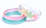 Two vibrant plastic bracelets from Lillies & Roses, the Starfish Blue Pink Bangles, are displayed overlapping on a white background. One features a playful mix of pink and green with glitter, while the other is clear and adorned with star-shaped charms in yellow, green, and pink. Handmade in Brazil, these whimsical accessories capture the joyful spirit of beach jewelry and evoke the dreamy charm of starfish-inspired bangles.