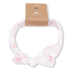 Angel Dear Knot Headband—white with light pink patterns, tied in a front bow. A cute baby accessory for fall and winter, displayed with a brown "Angel Dear" cardboard tag.