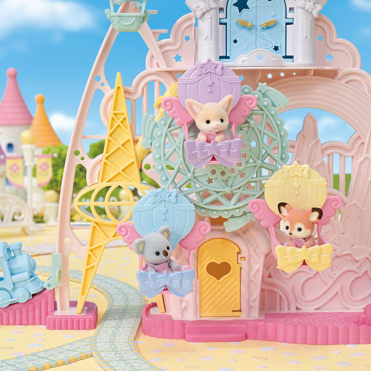 Three adorable small animal figurines from the Calico Critters brand sit in pastel balloon-shaped seats on the whimsical Ferris wheel of the Baby Dream Amusement Park playset, surrounded by a charming castle toy and creating a magical miniature fantasy-themed scene.