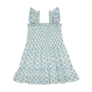 The Mer Girls' Paloma Dress is a sleeveless white dress featuring a blue and green tree print, with ruffled shoulder straps, a gathered bodice, twirly ruffle skirt, and a tiered ruffle hem, shown laid flat on a white background.
