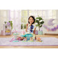 A young girl sits on a purple rug, smiling and playing with the Calico Critters Woodland Wonder Fairy Castle and enchanting fairy accessories in a brightly lit room with plants and pastel decor.