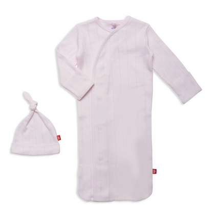 The Magnetic Me Baby Love Lines Gown + Hat Set features a light pink organic cotton newborn sleeper gown with long sleeves and magnetic closures, paired with a matching knotted hat, both displayed on a white background.