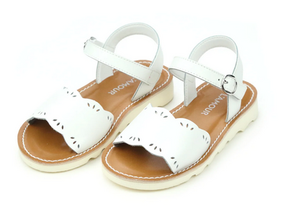 The Girls' Ella Scalloped Sandals by L'Amour Shoes feature white scalloped edges, ankle straps, and brown insoles for a cheerful touch. These feminine children’s sandals are shown on a white background.