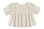 The Girls’ Colette Top by Rylee & Cru is a cream-colored, short-sleeved blouse adorned with a delicate floral pattern, gathered smocked detailing on the chest, and ruffled cuffs for a flattering fit.