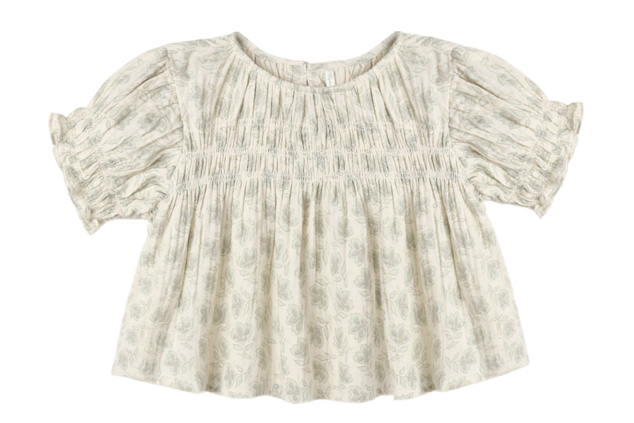 The Girls’ Colette Top by Rylee & Cru is a cream-colored, short-sleeved blouse adorned with a delicate floral pattern, gathered smocked detailing on the chest, and ruffled cuffs for a flattering fit.