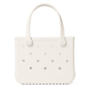 The Bitty Bogg® Bag by Bogg Bags is a white, rectangular tote featuring round side holes, sturdy handles, and the “bogg” logo embossed near the bottom corner. This compact tote is ideal for carrying daily essentials, and its washable design ensures easy cleaning and long-lasting durability.