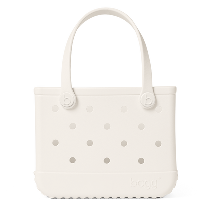 The Bitty Bogg® Bag by Bogg Bags is a white, rectangular tote featuring round side holes, sturdy handles, and the “bogg” logo embossed near the bottom corner. This compact tote is ideal for carrying daily essentials, and its washable design ensures easy cleaning and long-lasting durability.