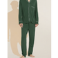A man wearing the Eberjey Willam Long PJ Set, a dark green men’s pajama with white piping made from sustainable TENCEL™ Modal, stands barefoot on a light background.