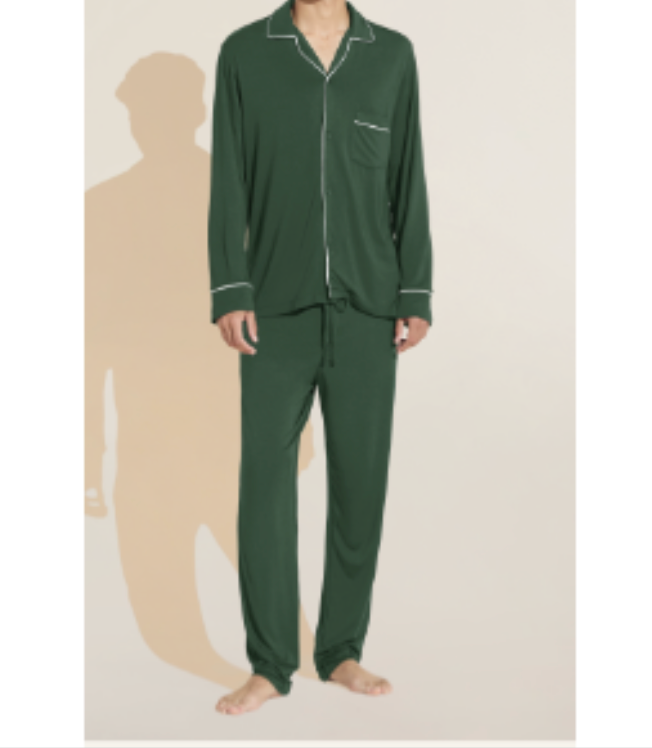 A man wearing the Eberjey Willam Long PJ Set, a dark green men’s pajama with white piping made from sustainable TENCEL™ Modal, stands barefoot on a light background.