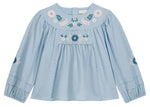 The Girls’ Risa Blouse by Louise Misha is crafted from light blue cotton and linen, adorned with floral embroidery on the chest and sleeves. It features scalloped trim, gathered cuffs, and subtly puffy sleeves for a delicate finish.