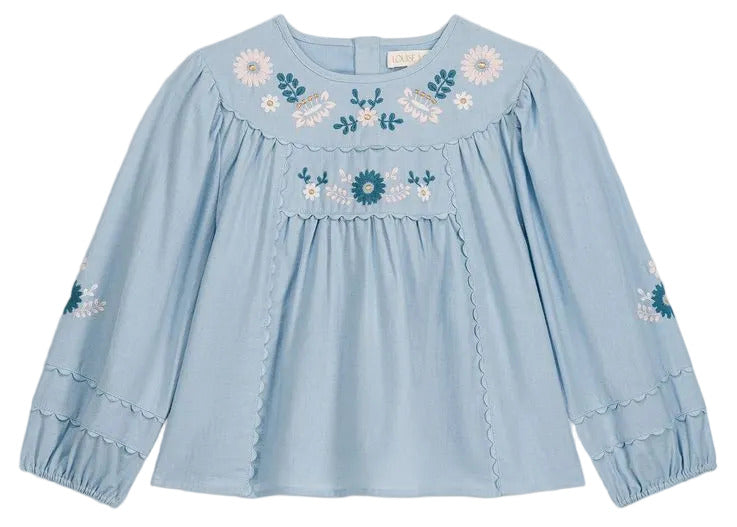 The Girls’ Risa Blouse by Louise Misha is crafted from light blue cotton and linen, adorned with floral embroidery on the chest and sleeves. It features scalloped trim, gathered cuffs, and subtly puffy sleeves for a delicate finish.