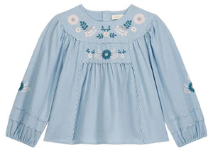 The Girls’ Risa Blouse by Louise Misha is crafted from light blue cotton and linen, adorned with floral embroidery on the chest and sleeves. It features scalloped trim, gathered cuffs, and subtly puffy sleeves for a delicate finish.