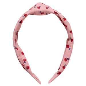 The Holly Headband from Pink Chicken showcases a pink fabric, a knotted top, and a lively floral pattern in red and dark blue.