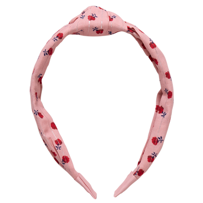The Holly Headband from Pink Chicken showcases a pink fabric, a knotted top, and a lively floral pattern in red and dark blue.