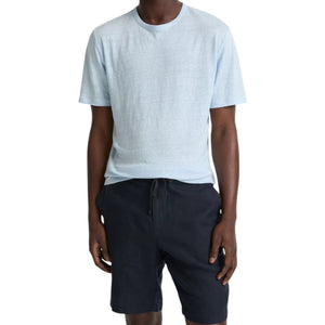 A person wearing the vince Linen Jersey Shortsleeve Crew in light blue and dark navy shorts stands against a plain white background.
