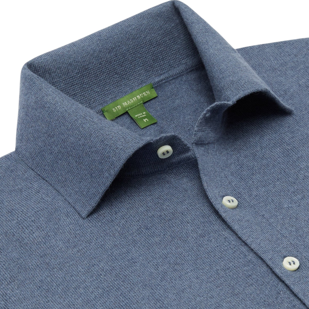 Close-up of the Sid Mashburn Long-Sleeved Rally Polo Sweater in blue, featuring a textured knit, spread collar, and white buttons, crafted from high-twist cotton and displayed on a flat surface.