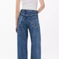 A person stands with their back to the camera against a plain light background, wearing a white sleeveless top and Rag & Bone Miramar Terry Sofie Full blue jeans.