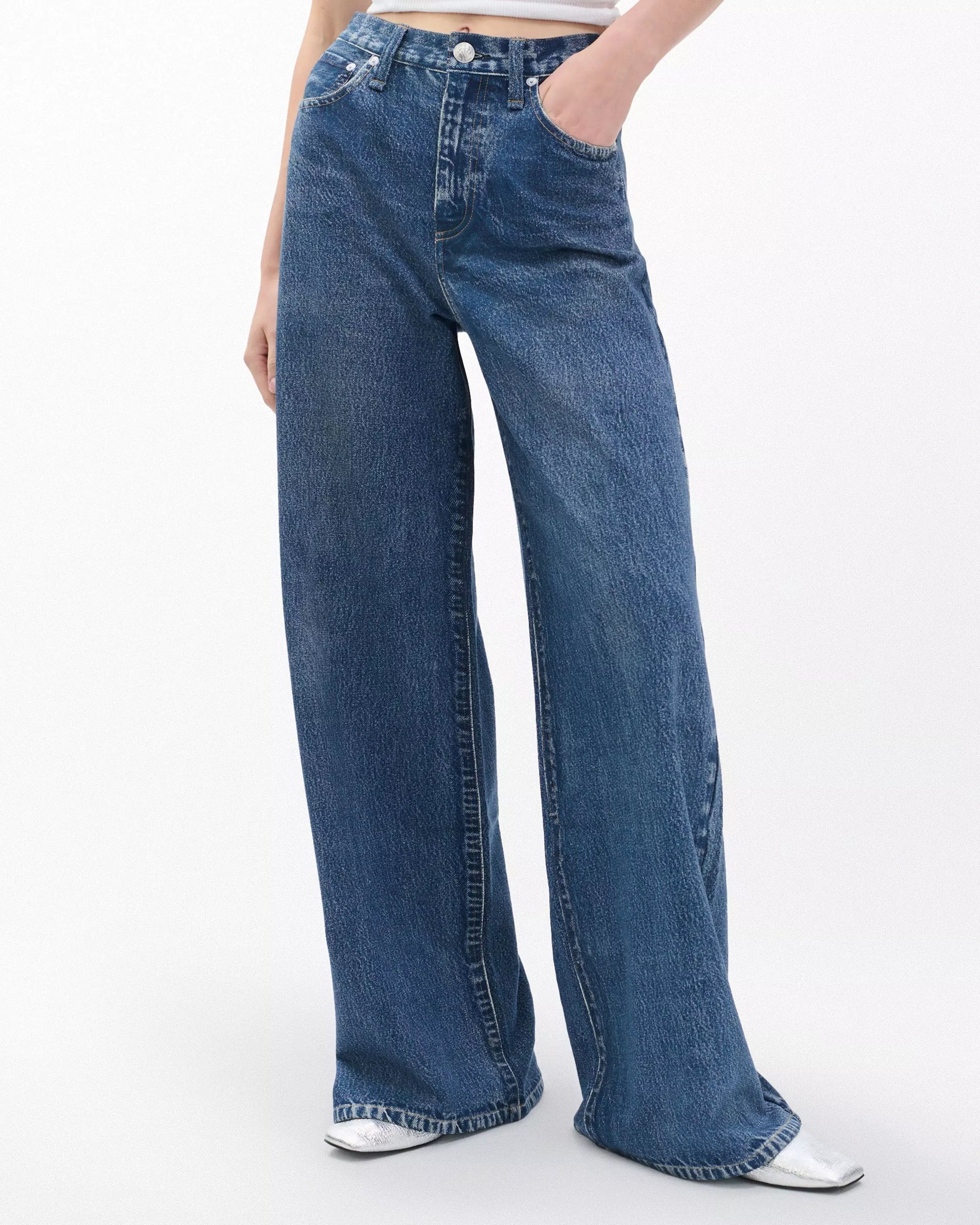 Person wearing Rag & Bone Miramar Terry Sofie Full high-waisted wide-leg blue jeans with white pointed-toe shoes, posed against a plain light background.