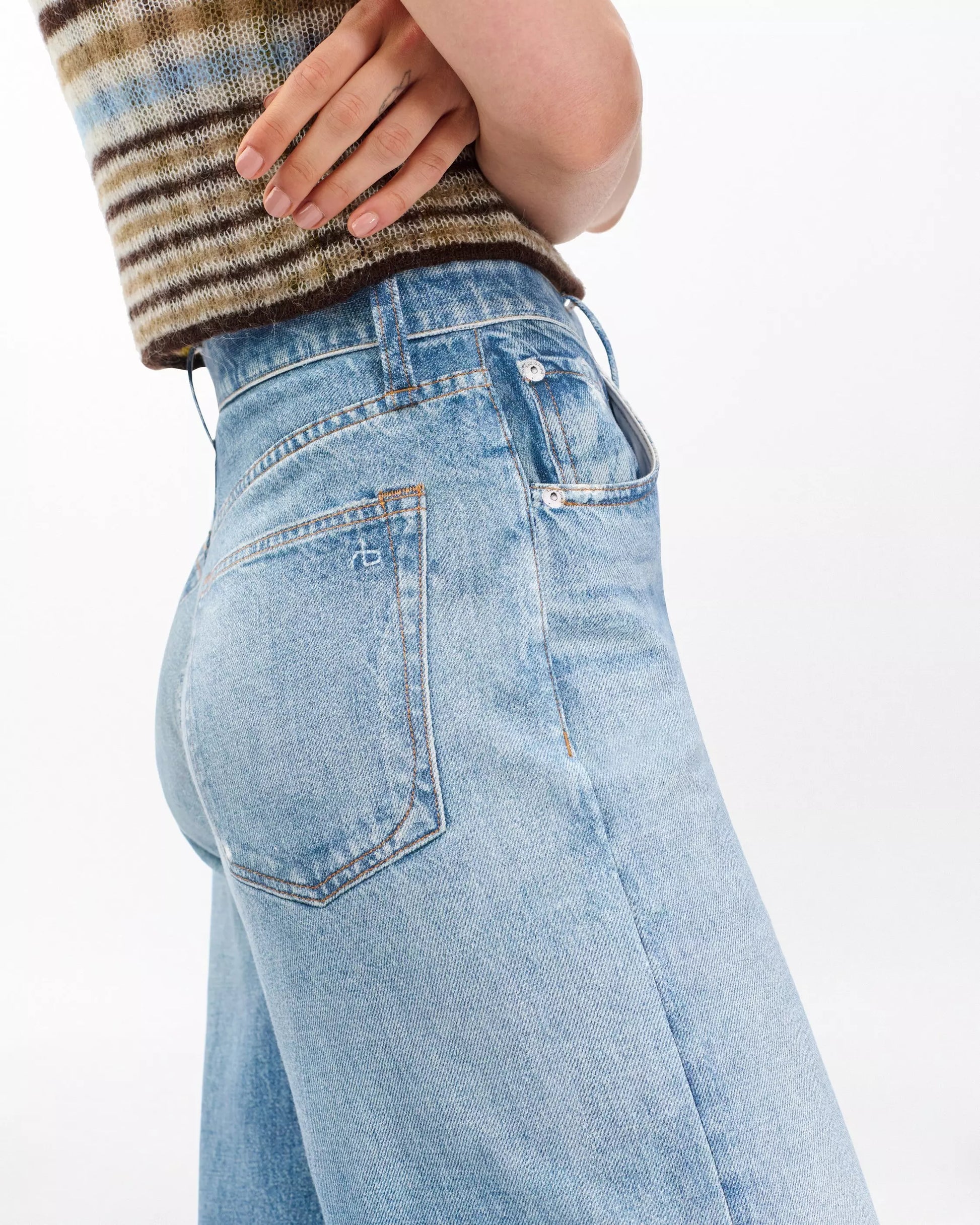 A person shown from the side and waist down wearing Rag & Bone's Miramar Terry Sofie Wide Pant in light blue with a brown and green striped sleeveless top.
