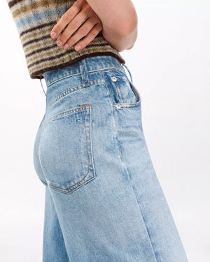 A person shown from the side and waist down wearing Rag & Bone's Miramar Terry Sofie Wide Pant in light blue with a brown and green striped sleeveless top.