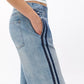 A person wearing Rag & Bone's Miramar Terry Wide Track Pant, featuring a wide-leg fit in light blue with dark blue side stripes, stands with one hand in their pocket against a plain white background.